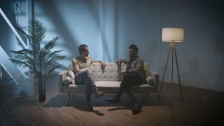 Two men on a couch interview scene, talking and sharing stories, podcast concept.