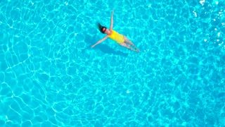 View from the top as a woman in a yellow swimsuit lying on her back in the pool. Relaxing concept